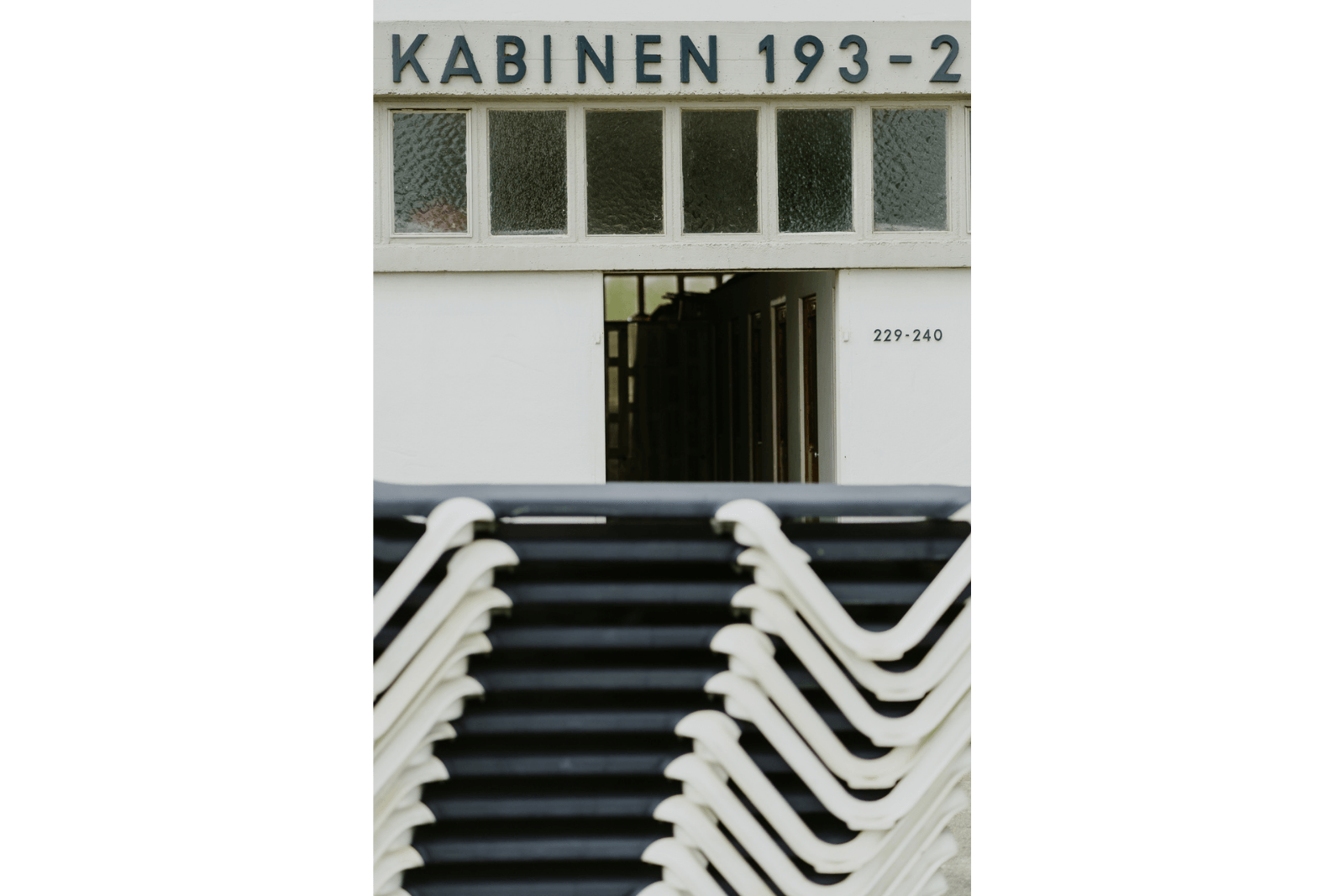 Stapeln von blauen Liegestühlen im Vordergrund, dahinter die Kabinen des Badehauses