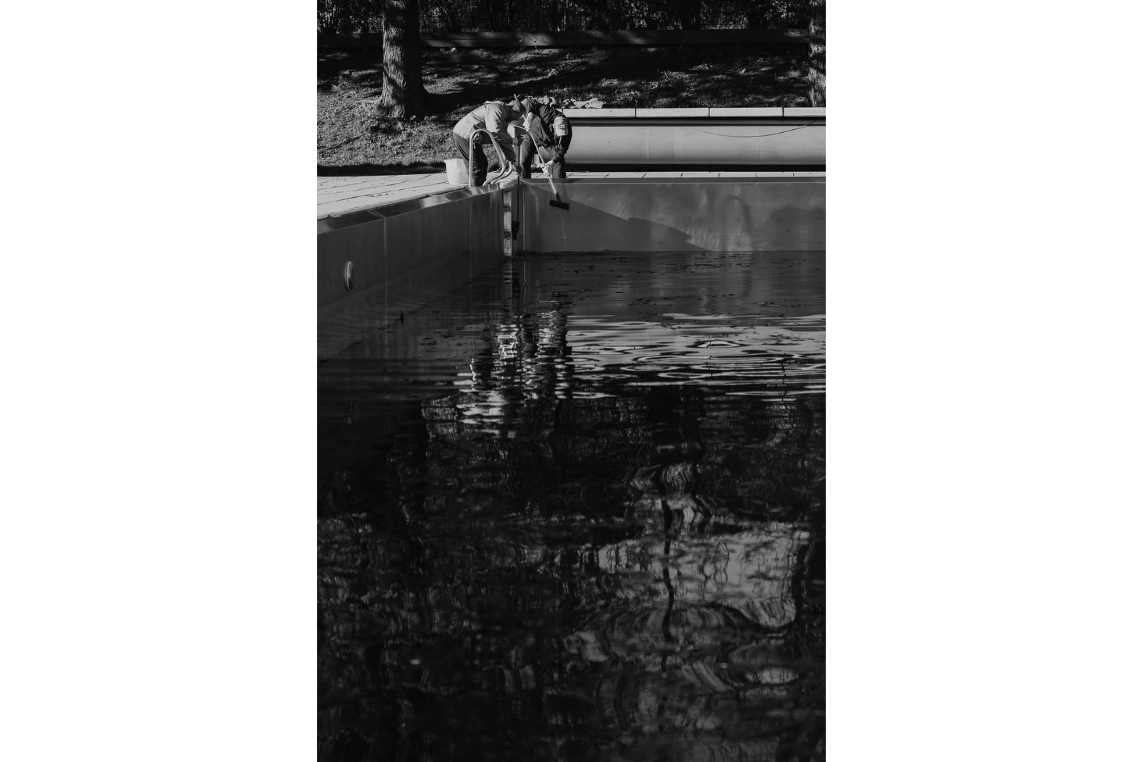 Schwarzweiß Fotogtafie. Mitarbeiter des Strandbads Alte Donau fischen mit Kescher Verunreinigungen aus dem Schwimmbecken. Fotoprojekt, Fotoreportage Wien