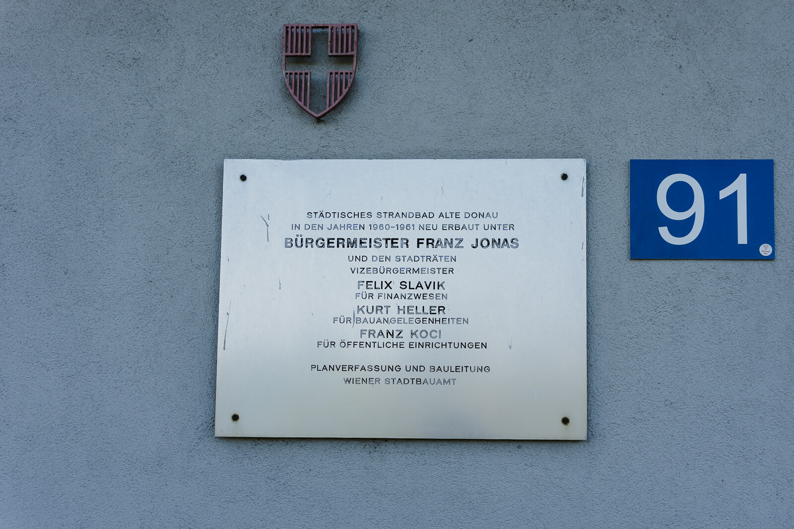 Schild, das über die Entstehung des Strandbads Alte Donau informiert. Dieses ist an der Mauer des Eingangsbereichs angebracht. Fotoprojekt, Fotoreportage Wien