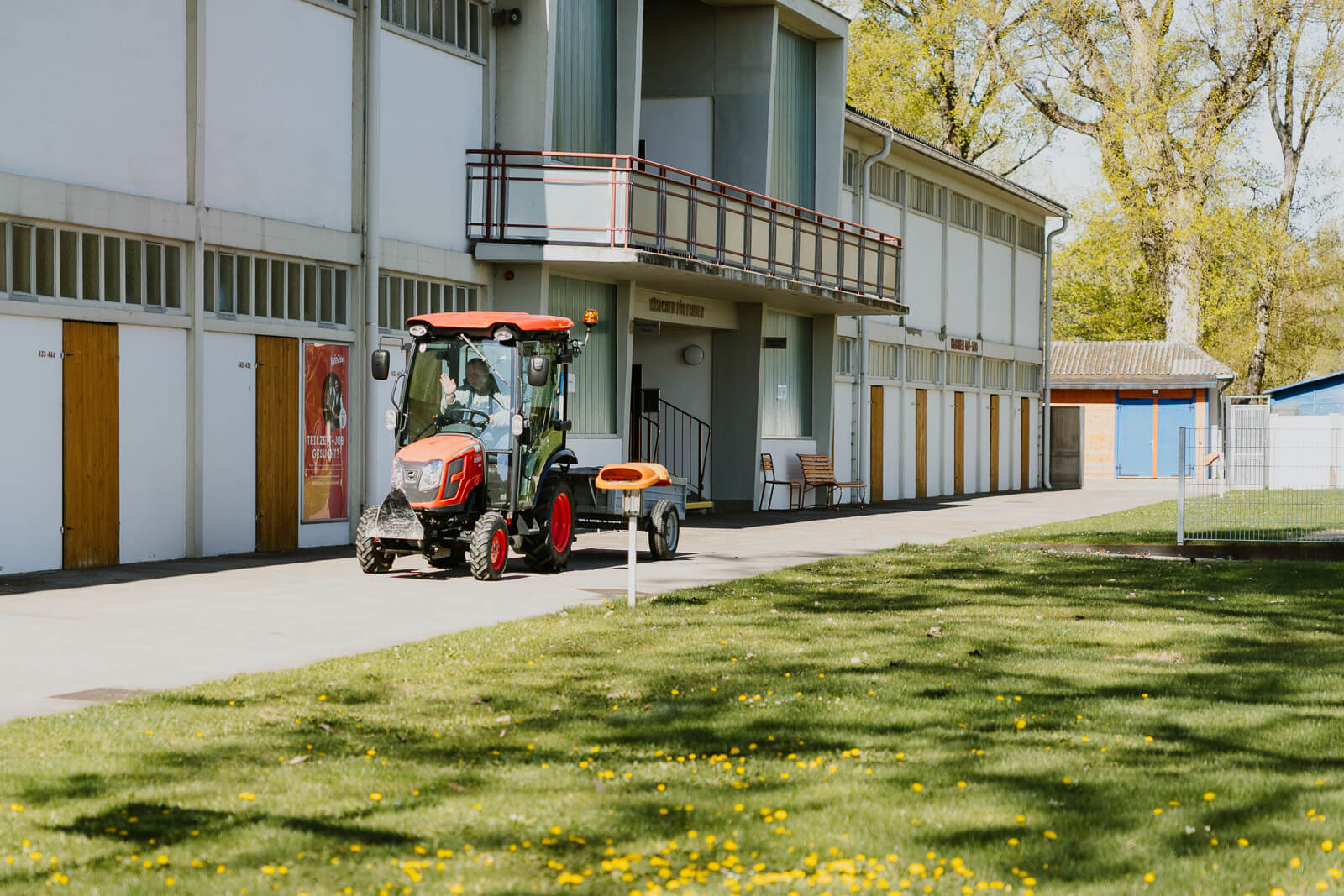 Außenansicht des Badehauses im Strandbad Alte Donau. Ein kleiner Mähtraktor fährt gerade vor dem Haus vorbei, der Fahrer winkt.