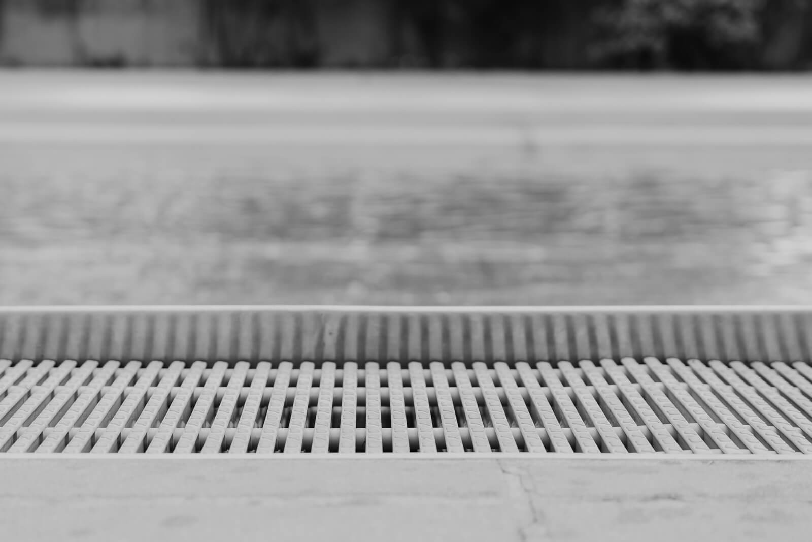 Schwarzweißfotografie eines Schwimmbeckens. Detailaufnahme des Wassers und Beckenrands.