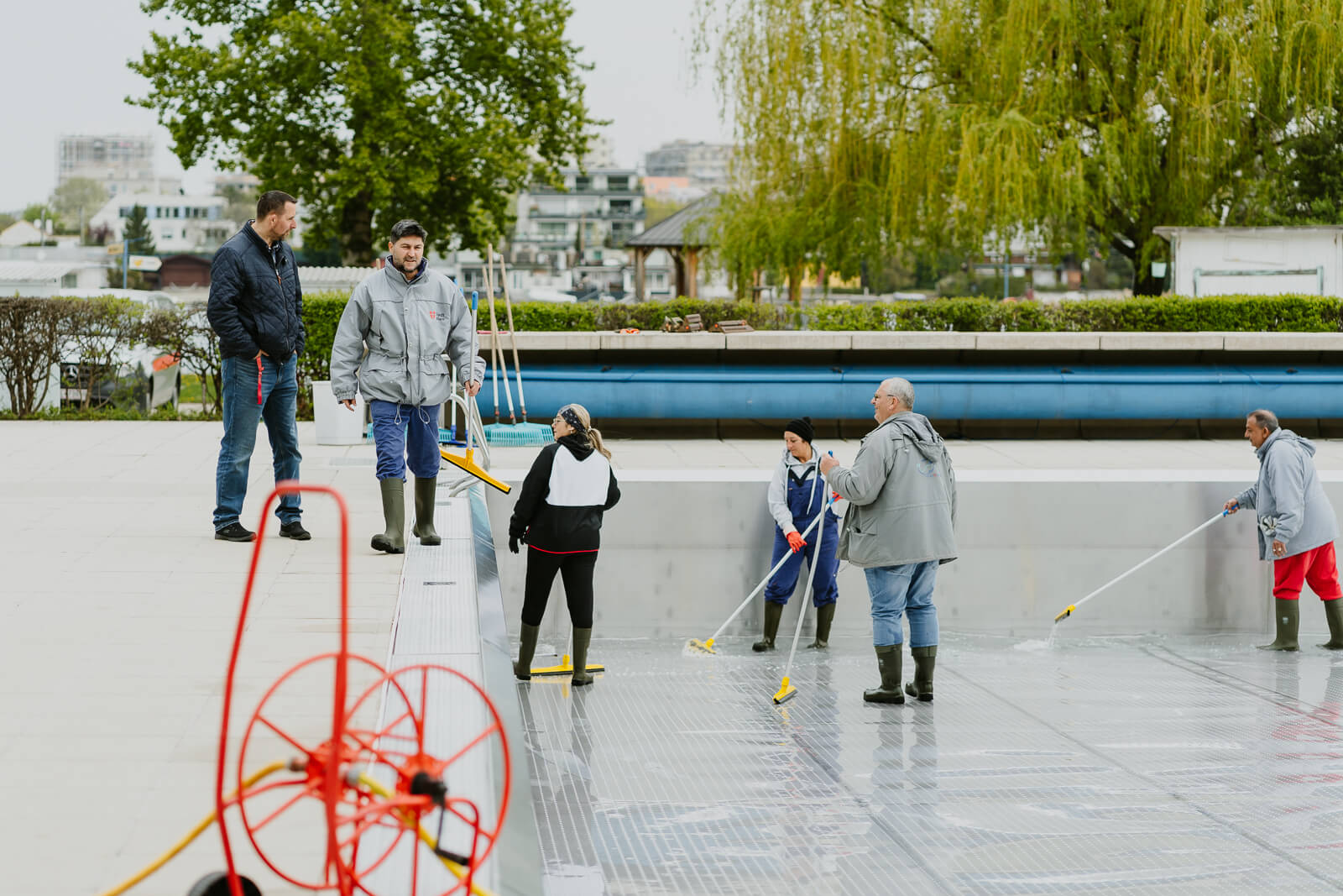 Die Mitarbeiter:innen des Bads unterhalten sich ein wenig während der Arbeit. Ein paar Menschen stehen am Beckenrand, ein paar Menschen befinden sich in den Becken.