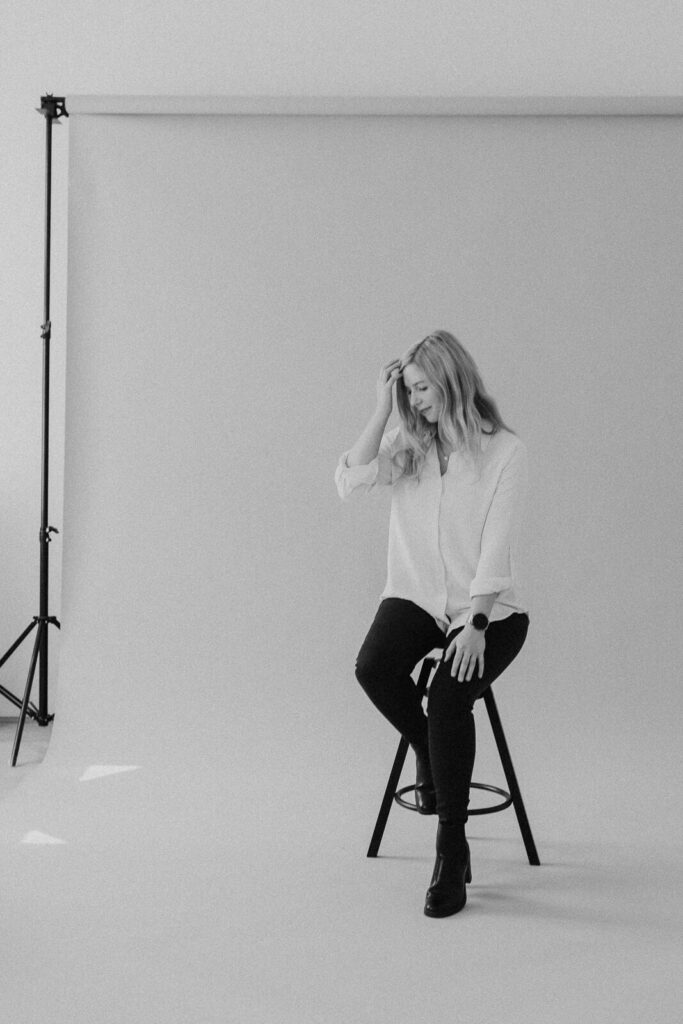 Frau sitzt auf einem Hocker im Studio, schwarz-weiß Portrait mit natürlichem Ausdruck – Personal Branding Fotografie Wien und Niederösterreich