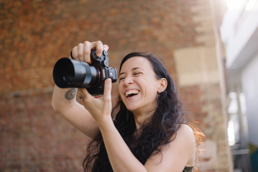 Fotografin Anna Sommerfeld fotografiert lachend im Außenbereich, lebendige und authentische Arbeitsszene